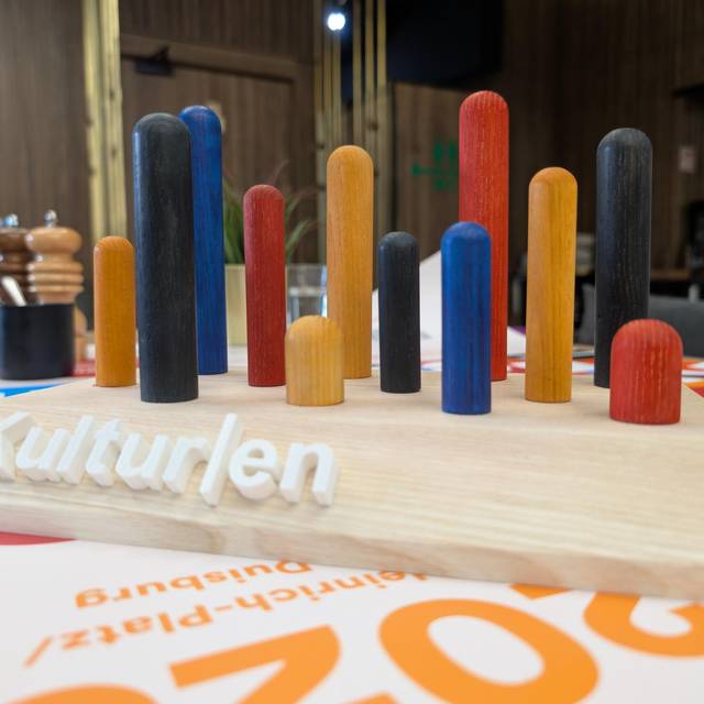 Eine Holzplatte mit bunten Stäben in verschiedenen Farben, die herausragen. So sieht der DU-Kulturen-Award aus.