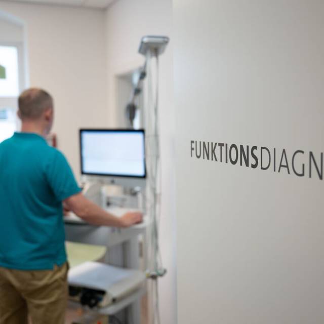 Ein Arzt führt in ein Behandlungszimmer ein funktionelles Gerät. Auf einer Schrift steht Funkionsdiagnostik.