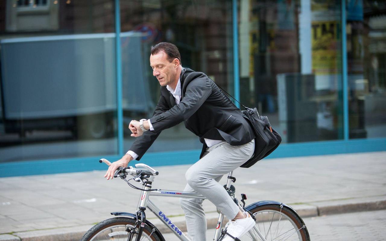 Mann fährt mit Fahrrad durch Stadt und guckt auf Uhr