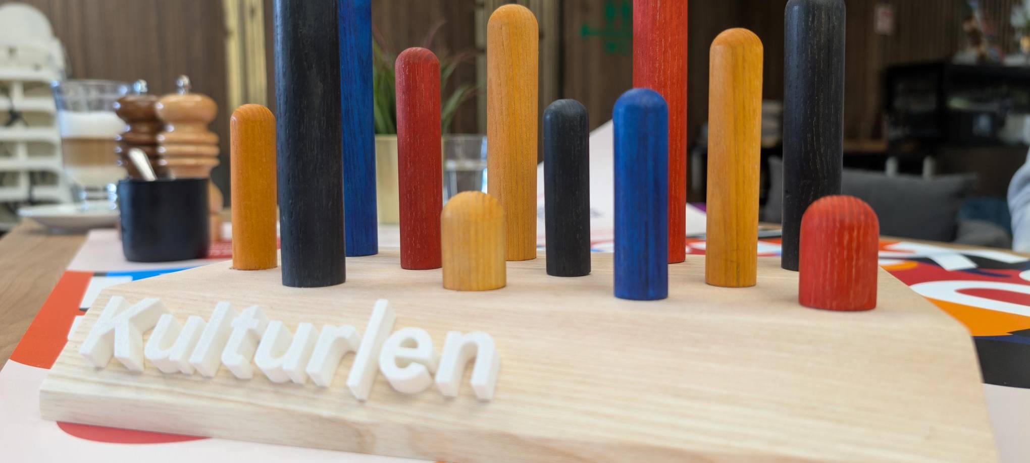 Eine Holzplatte mit bunten Stäben in verschiedenen Farben, die herausragen. So sieht der DU-Kulturen-Award aus.