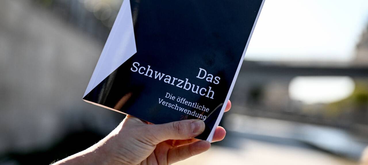 Das Schwarzbuch 2025/26 vom Bund der Steuerzahler in wird vor das Reichstagsgebäude gehalten. Das Schwarzbuch listet Beispiele auf, wo aus Sicht des Steuerzahlerbunds Steuergelder verschwendet wurden.