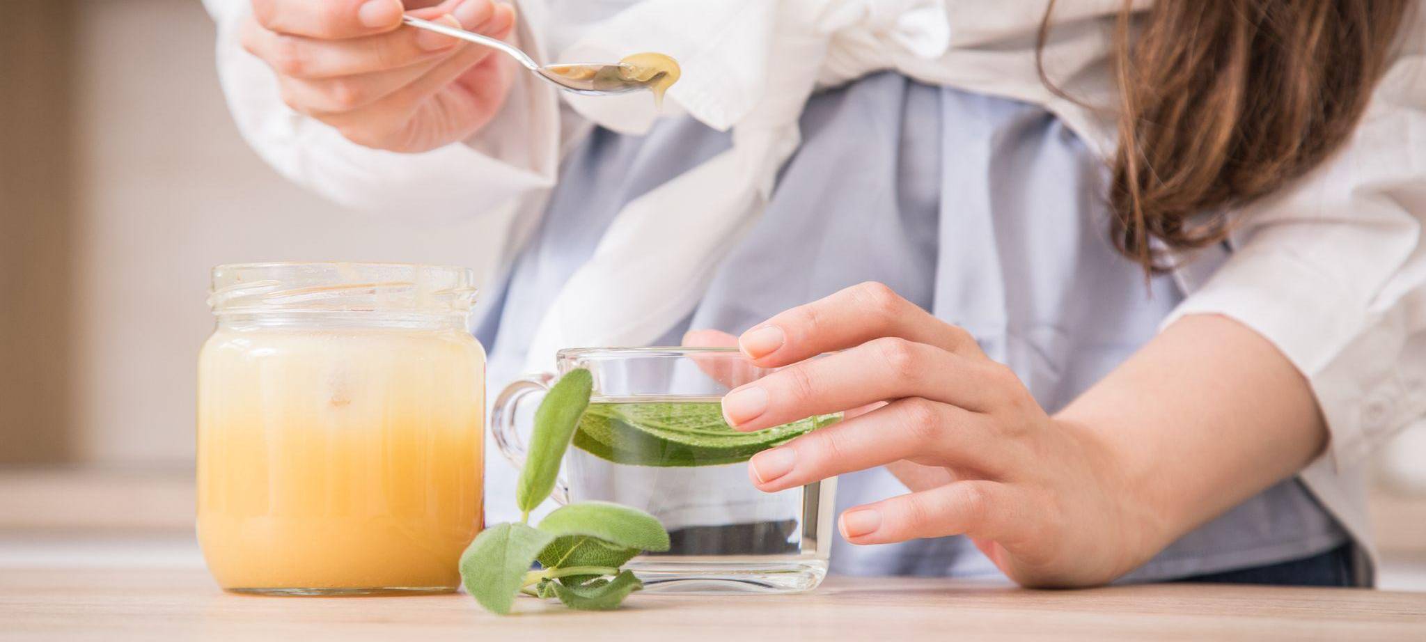 Eine Frau bereitet frischen Salbeitee mit Honig zu