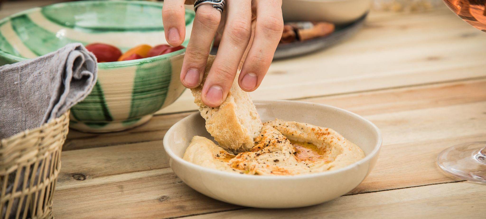 Ein Mann dippt ein Stück Brot in Hummus