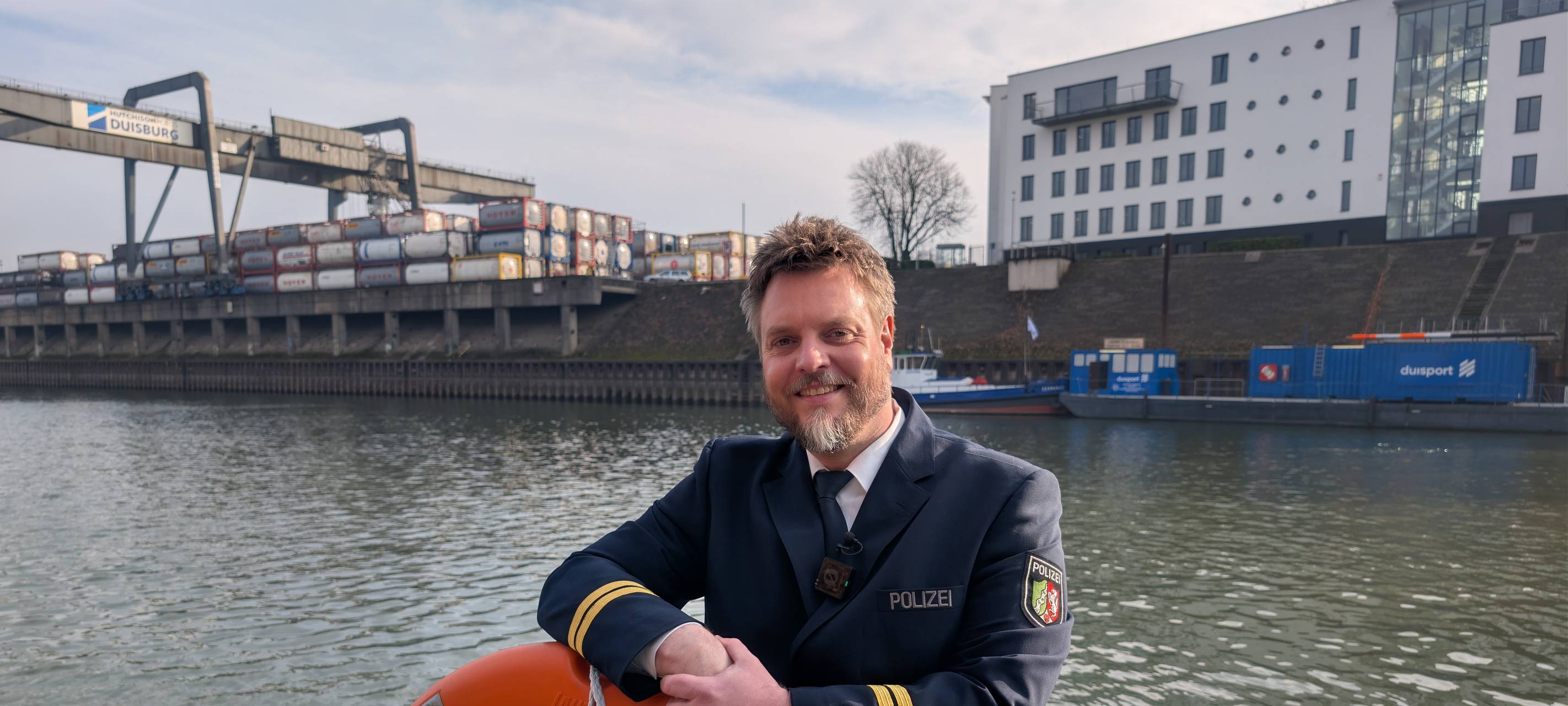 Polizeioberkommissar Dennis Fresdorf posiert an der Reling eines Polizeibootes mit einem Rettungsring.