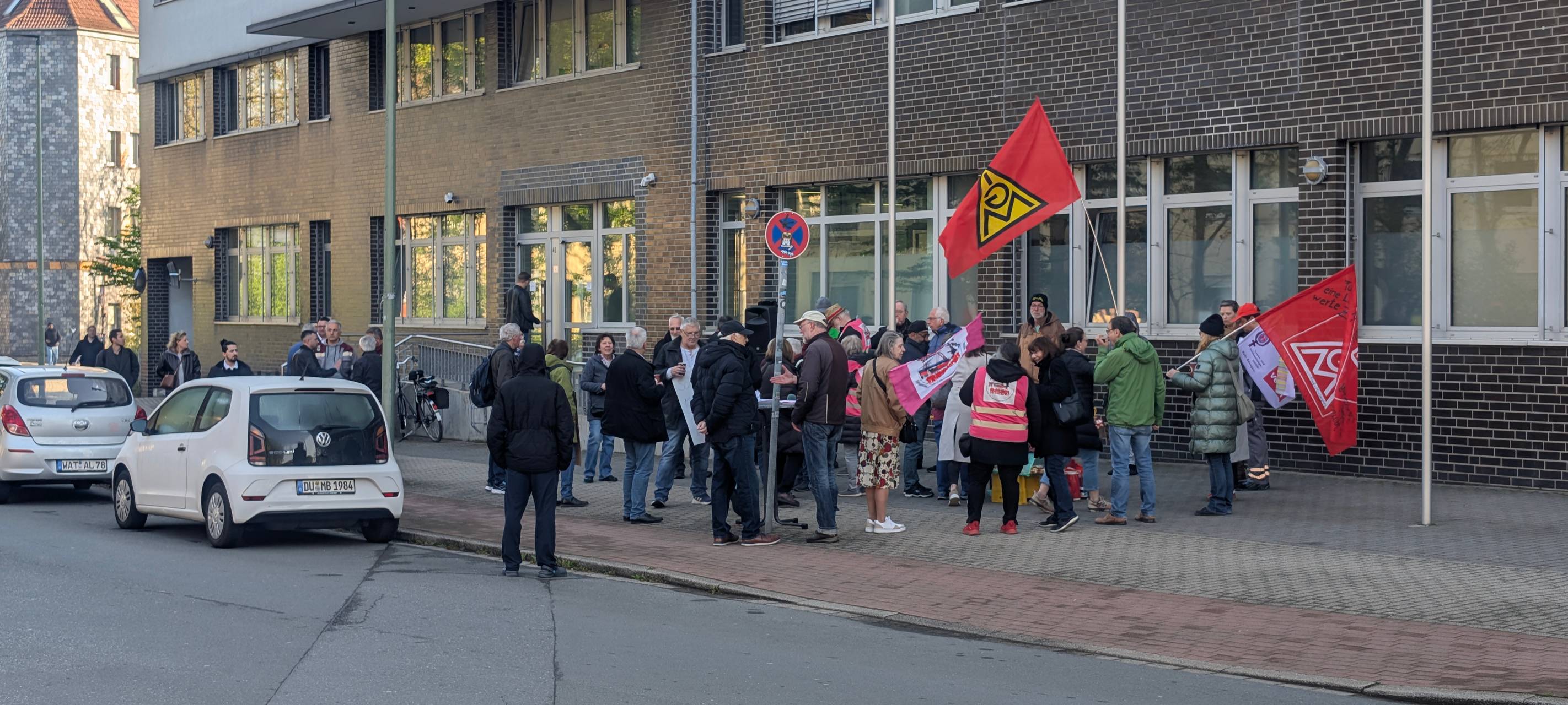 Rund 40 Leute solidarisieren sich bei einer Kundgebung mit dem Kläger Markus Stockert, halten Fahnen der Gewerkschaft IG Metall und zeigen Plakate mit Solidaritätsbekundungen.