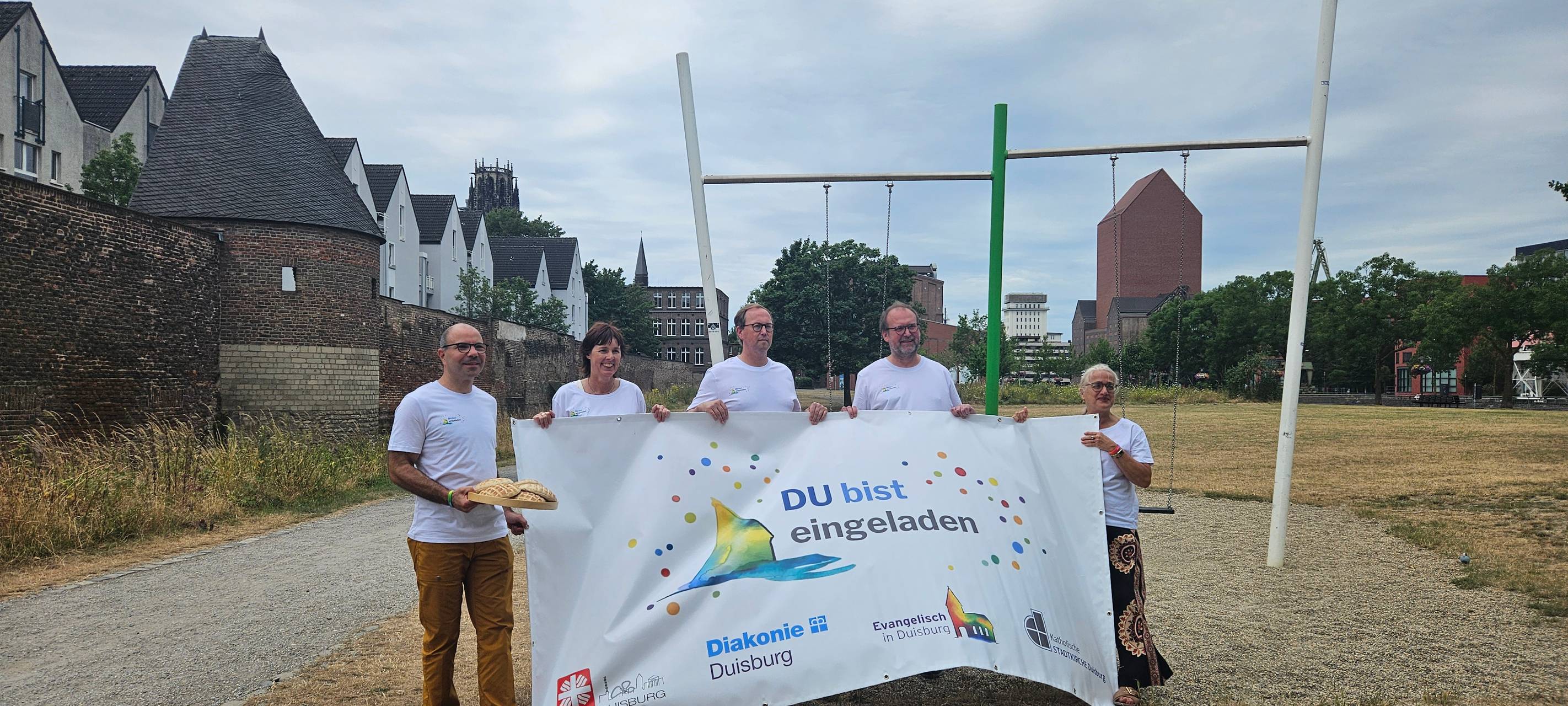 Organisatoren der Kirchen und Wohlfahrtsverbände in Duisburg halten Plakat mit Aufschrift "DU bist eingeladen" in Duisburg